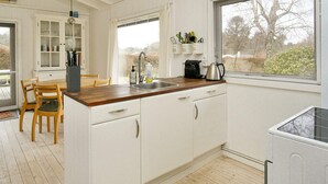 Una cocina con armarios blancos, encimera de madera, un fregadero y una ventana con vistas a árboles.