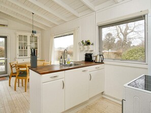 Una cocina con armarios blancos, encimera de madera, un fregadero y una ventana con vistas a árboles.
