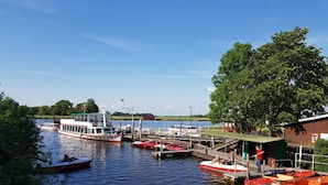 A riverside dock with boats, a pier, and a building with a green roof. - Haus Limosa Comfortable Holiday Residence (Friedrichstadt)