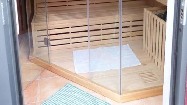 A sauna room with a wooden interior, a glass door, and a tiled floor. - Haus Limosa Comfortable Holiday Residence (Friedrichstadt)