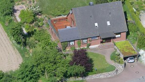 An aerial view of a house with a sloped roof, a visible chimney, and a paved driveway leading to a garage. - Holiday Apartment Erika Leonhardt (Dersau)