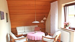 A cozy room with a wooden ceiling, a white sofa, a round table, and two chairs. - Holiday Apartment Erika Leonhardt (Dersau)