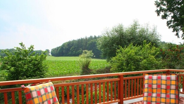 A wooden deck with a table and chairs, overlooking a green field and trees. - Holiday Apartment Erika Leonhardt (Dersau)