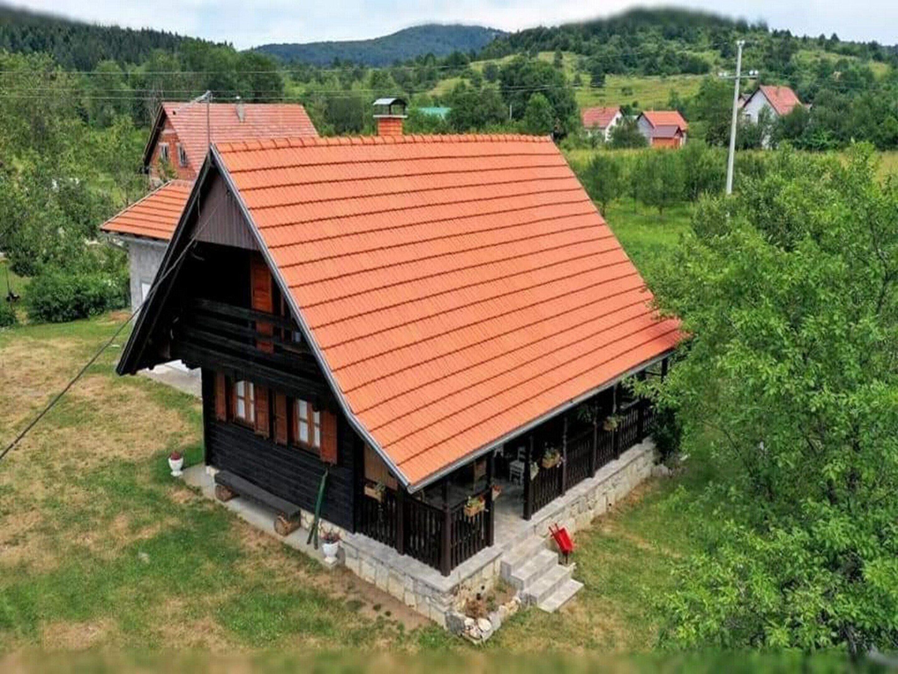 Una casa de madera tradicional con techo rojo inclinado, rodeada de vegetación y colinas al fondo.