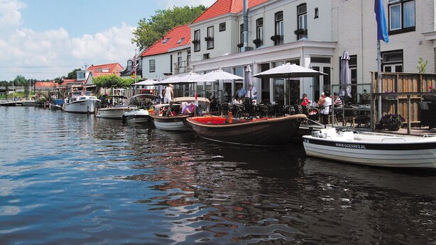 A waterfront area with boats docked along the water, a row of buildings with red roofs, and outdoor seating areas with umbrellas. - Spacious Holiday Home With Outdoor spa (Akkrum)