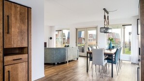 A modern kitchen with wooden cabinetry, a dining area with a table and chairs, and a large sliding glass door leading to a balcony. - Spacious Holiday Home With Outdoor spa (Akkrum)