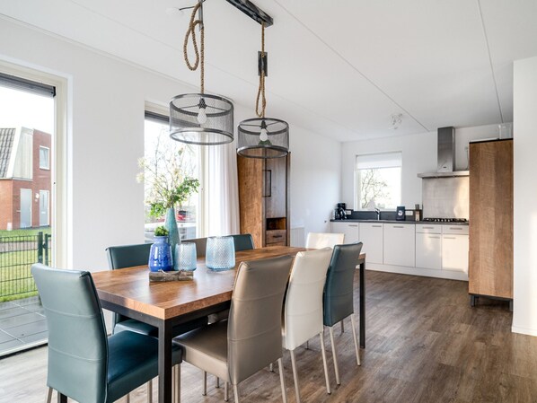 Une cuisine moderne avec des meubles blancs, une table à manger en bois et une vue sur l’extérieur.