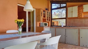 A kitchen with wooden cabinets, a white table, and chairs. There is a window with a view of trees and a clock on the wall. - Comfortable Apartment With Private Terrace (Fazana)