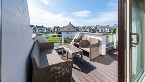 Een balkon met rieten meubilair, uitzicht op woongebouwen en een heldere lucht.