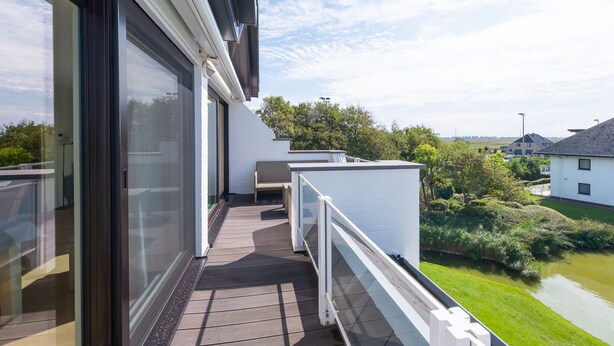 A balcony with a view of a river and greenery, a white building, and a clear sky. - Attractive Apartment With Magnificent View (Middelkerke)