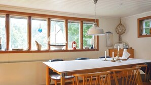 A dining area with a wooden table and chairs, large windows with curtains, and a hanging light fixture. - 6 Person Holiday Home in Munkedal-by Traum (Munkedal)