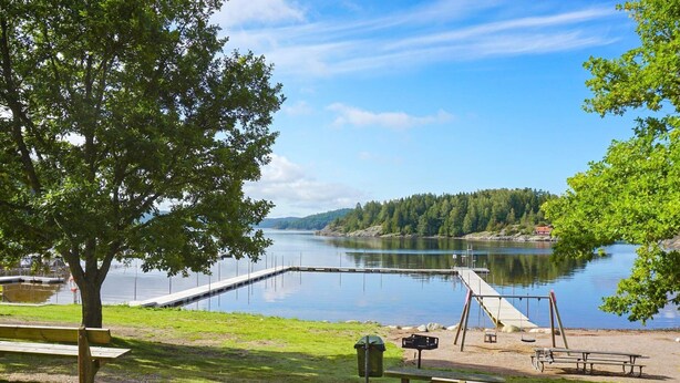 A lakeside park with picnic tables, a wooden bench, a swing set, and a dock extending into the water. - 6 Person Holiday Home in Munkedal-by Traum (Munkedal)