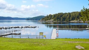 A lakeside view with a dock, grassy area, and a forested hill in the background. - 6 Person Holiday Home in Munkedal-by Traum (Munkedal)