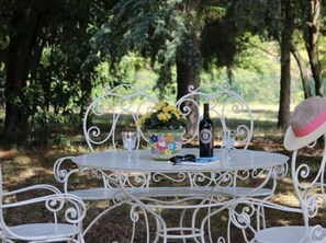 A white metal table with a floral vase, a bottle, and glasses set outdoors.