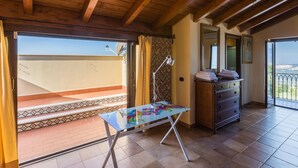Ein Zimmer mit Balkon, einem Tisch mit bunten Tischdecken, einer Lampe und einer Kommode mit Handtüchern.