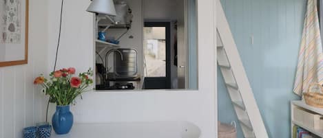 A room with a white table, a blue vase with flowers, a white chair, a bookshelf, and a staircase.