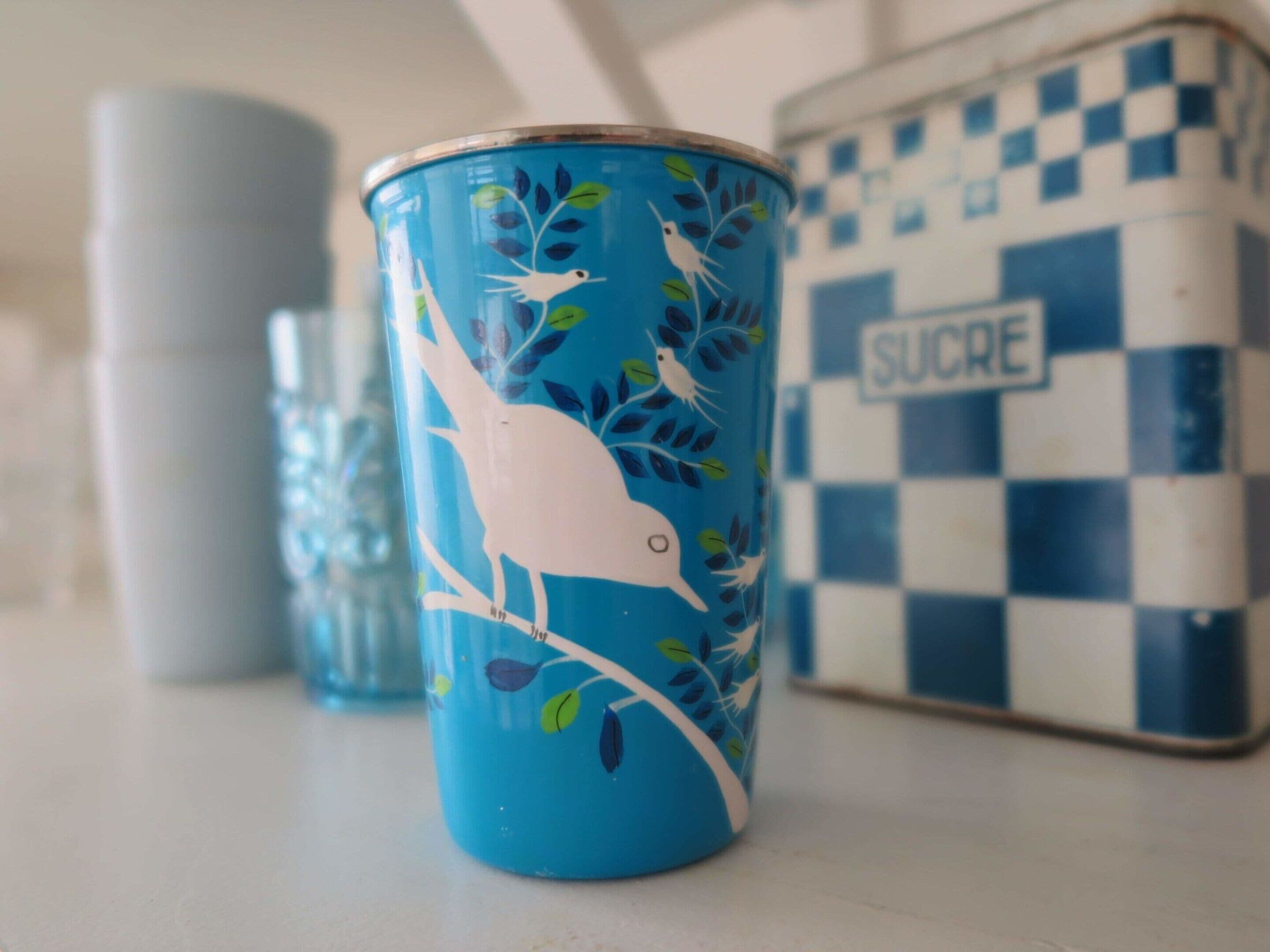 A blue mug with bird and leaf designs, a checkered sugar container, and a cylindrical container.