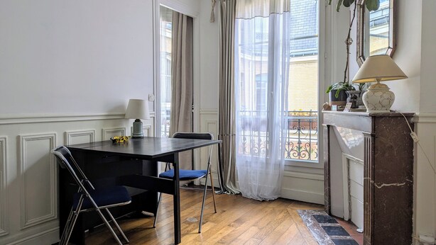 Une pièce avec un plancher en bois, une table à manger avec des chaises, une cheminée et une grande fenêtre avec des rideaux.