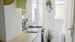 Une cuisine étroite avec un plan de travail en bois, des armoires blanches et un sol carrelé. Des fenêtres laissent entrer la lumière naturelle, et un ventilateur de plafond est visible.