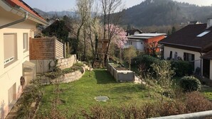 A residential area with houses, a well-maintained lawn, and a view of a forested hill in the background.