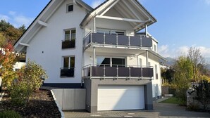 A two-story residential building with a white facade, a garage, and a balcony on the upper floor.