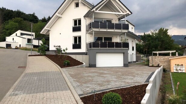 A modern two-story house with a garage, a balcony, and a landscaped front yard.