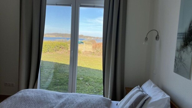 Een slaapkamer met een groot raam, een bed, een wandlamp en een schilderij.
