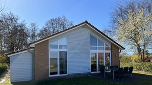 Een gelijkvloers huis met garage, grote ramen en een terras met stoelen.