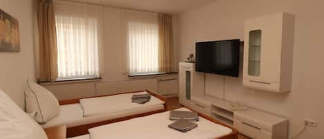 Una habitación de hotel con dos camas individuales, televisión, un mueble pequeño y un radiador.