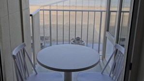 A balcony with a round table and two chairs, overlooking a beach with a fence and a clear sky. - Coastal Comfort With Views (Nieuwpoort)