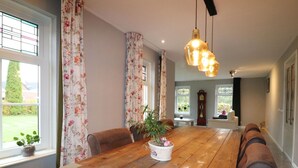 A dining area with a wooden table, floral curtains, and a hanging light fixture. - Apartment in Kornhorn Near Curringherveld (Kornhorn)