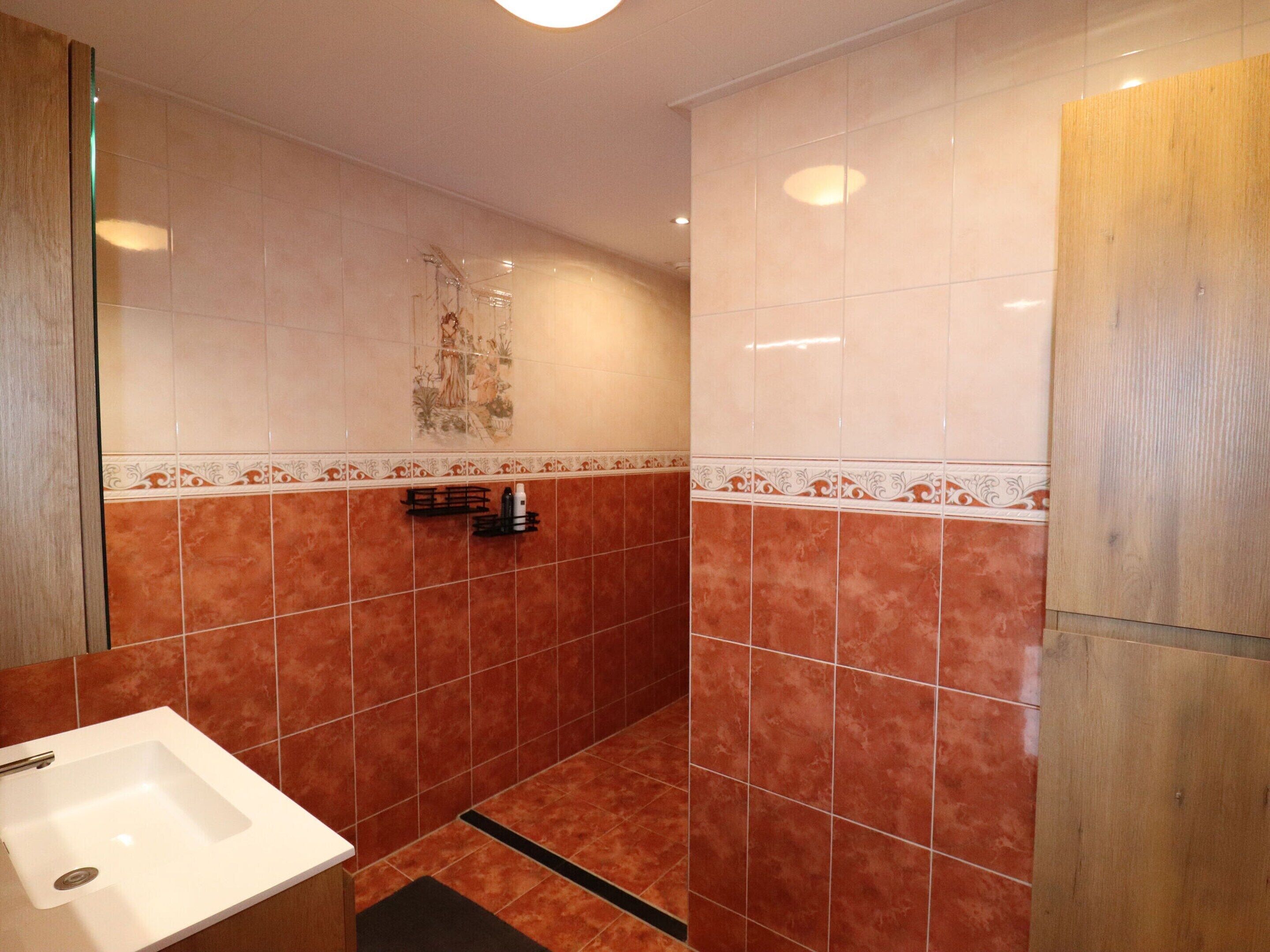 A bathroom with a white sink, a shower, and a tiled wall with a decorative border.