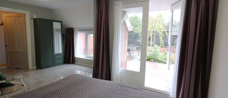 A bedroom with a large bed, a sliding glass door to a patio, a wardrobe, and a door leading to another room.