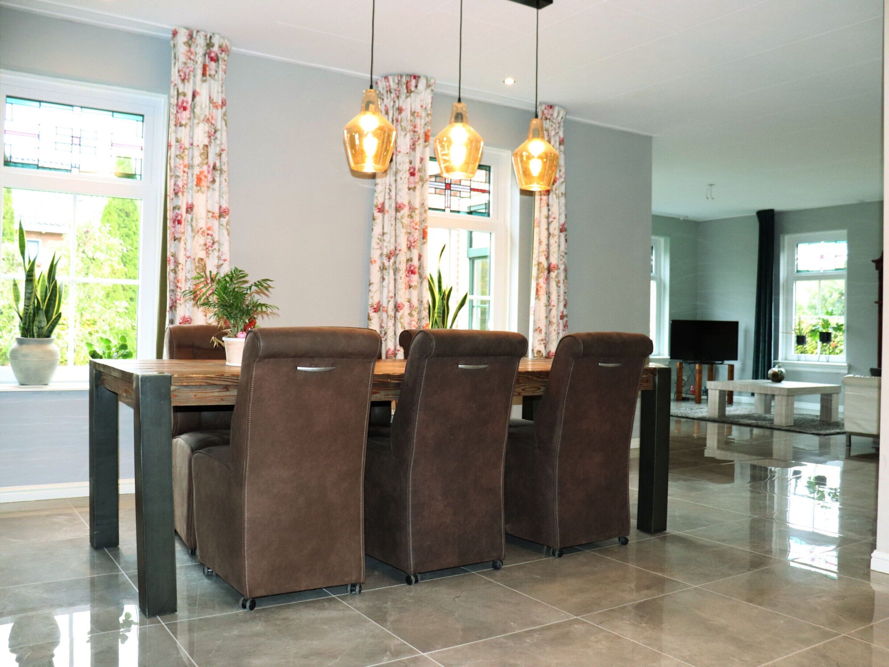 A dining area with a wooden table, four brown chairs, floral curtains, and pendant lights.