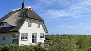 Ein Haus mit steilem Dach, weißen Außenwänden und einem Schornstein.