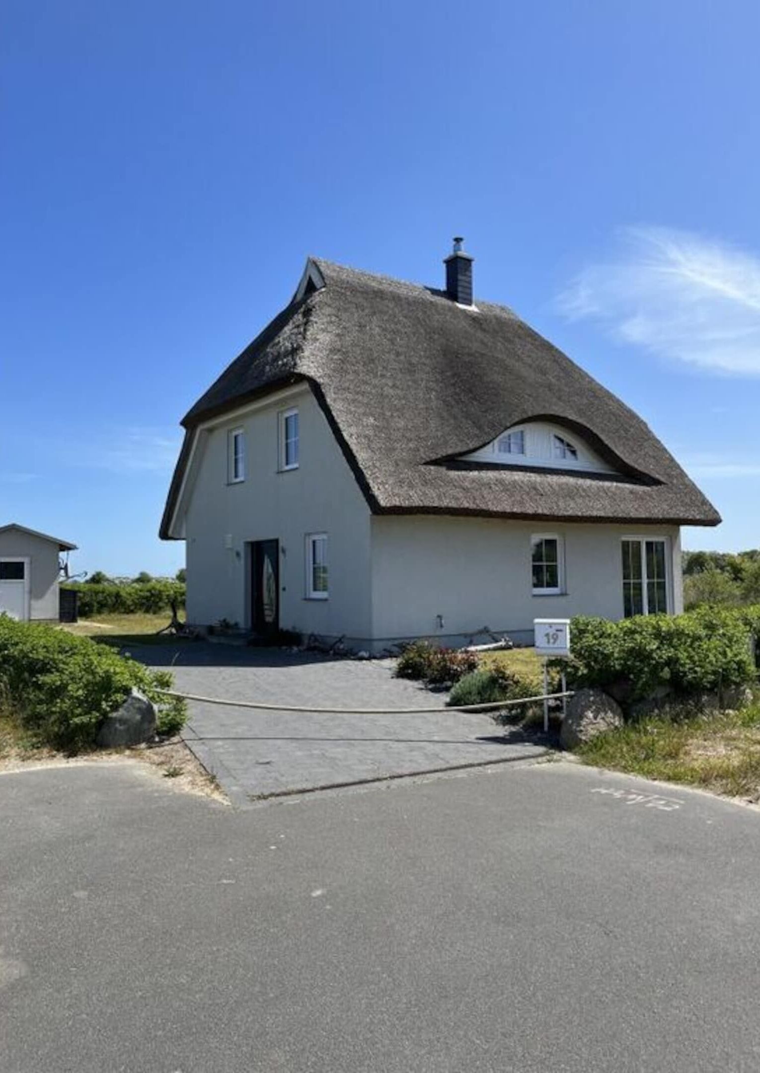 A single-story house with a thatched roof, a front door, and a number '19' sign.