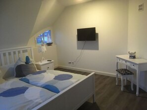 Ein Schlafzimmer mit einem Bett, einem Schreibtisch, einem Stuhl, einem Fernseher und einem Fenster.