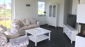 Ein Wohnzimmer mit einem blumigen Sofa, einem weißen Couchtisch, einem Schrank mit Glastüren und einem Fernseher.