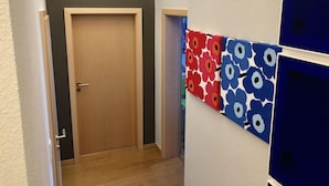 A hallway with a wooden door at the end, a white wall, and a blue and red floral-patterned partition. - Sea View and Design Comfortable Vacation Home (Sassnitz)