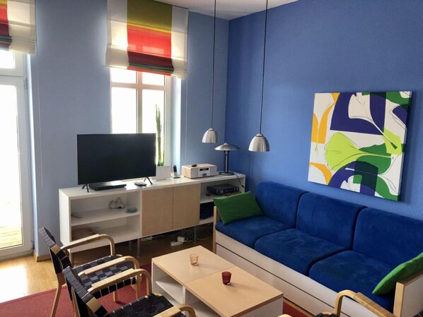 A modern living room with a blue sofa, a flat-screen TV, a coffee table, and a painting on the wall. - Sea View and Design Comfortable Vacation Home (Sassnitz)