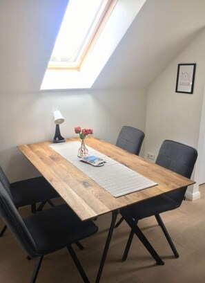 Un coin repas avec une table en bois, des chaises noires, une petite lampe et un vase avec des fleurs.