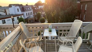 A balcony with two white metal chairs and a small table with a potted plant.