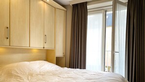 Ein ordentlich bezogenes Bett in einem Zimmer mit Holzschränken und einem großen Fenster mit Vorhängen.