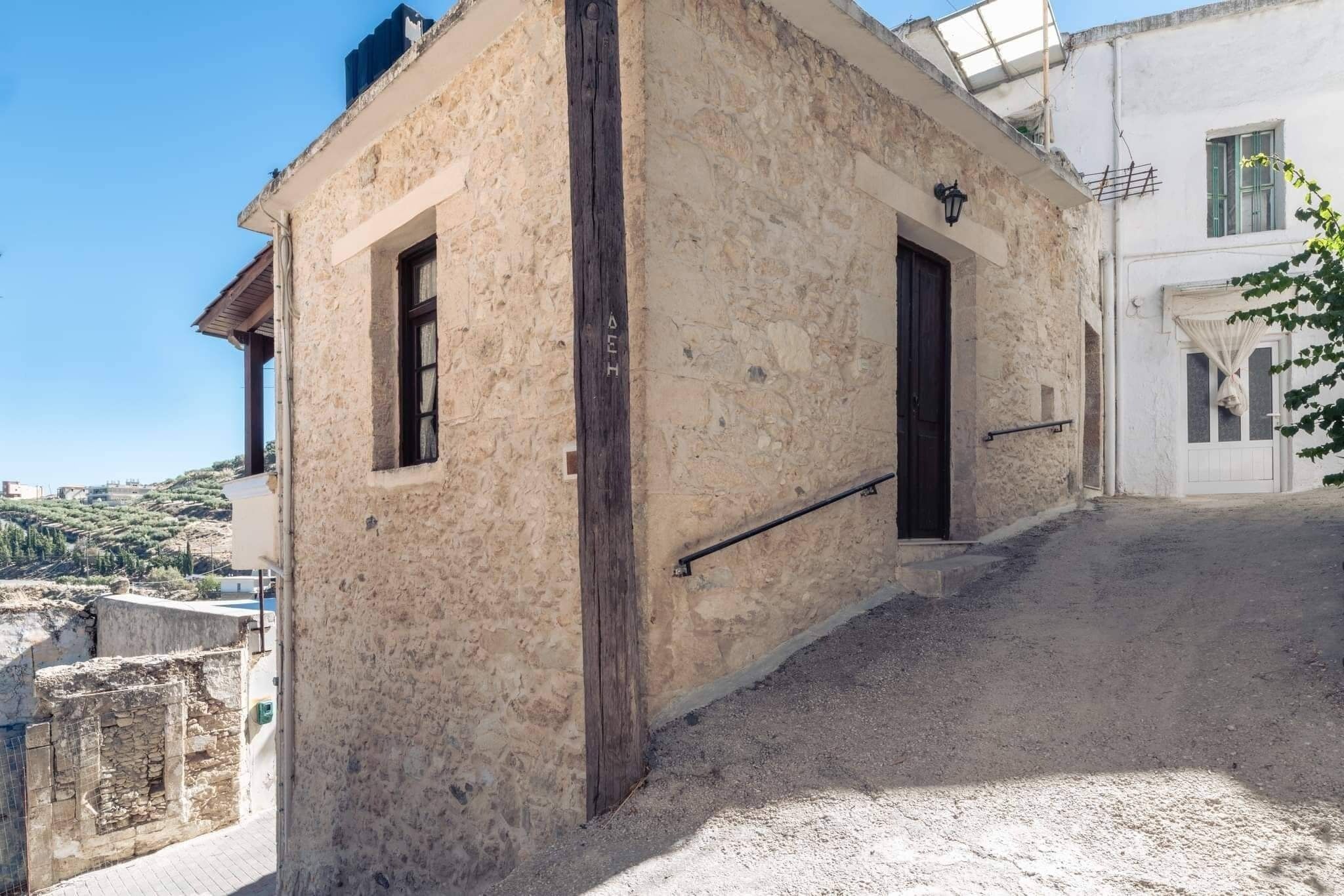 Um edifício de pedra com duas portas de madeira escura e uma pequena janela, situado em frente a um morro.
