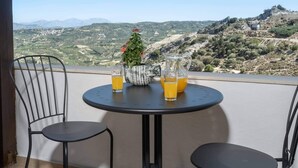 Een balkon met een tafel gedekt voor twee personen, een potplant en twee glazen jus d'orange.