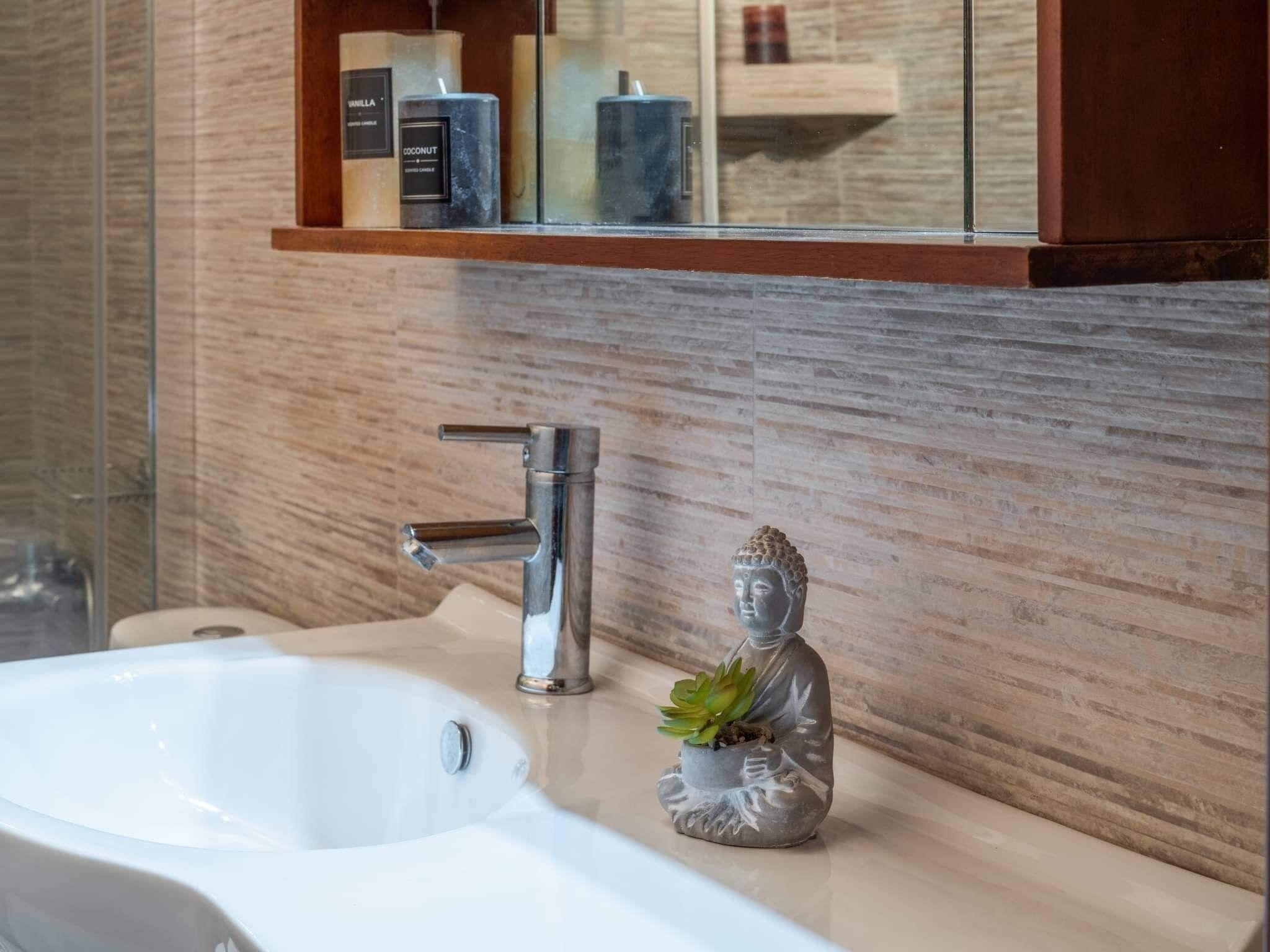 Een badkamer met een wit wastafel, een moderne kraan en een klein Boeddhabeeldje op het aanrecht.