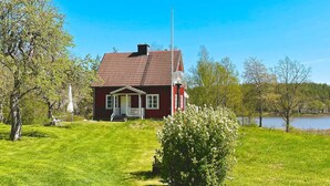A red house with a porch, a lawn, and a lake in the background. - 5 Person Holiday Home in Edsbruk-by Traum (Valdemarsvik)