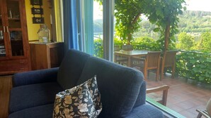 Ein Wohnzimmer mit einem dunkelblauen Sofa, einem Blumenkissen und Blick auf eine grüne Landschaft durch große Fenster.