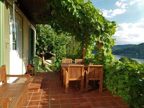 A covered patio with wooden furniture and a view of a lake. - Holiday Home Lake View (Unterwellenborn)