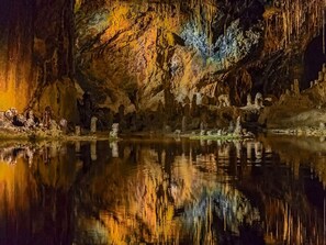 A cave with stalactites and stalagmites, a calm pool of water reflecting the cave's interior, and a rocky shore. - Holiday Home Lake View (Unterwellenborn)